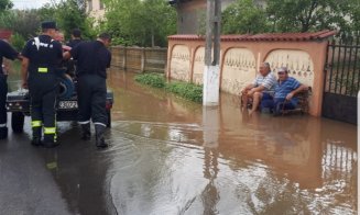 Fotografia zilei: doi localnici stau pe bancă în timp ce pompierii scot apa din comună