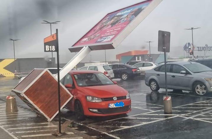 Panou publicitar CĂZUT peste mașina unui clujean în parcarea unui mall